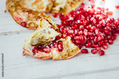 Pomegranate peel and seeds over white wooden background.
