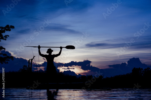 Zdjęcie XXL Sylwetka rybak pozycja na łodzi, chwyta paddle, na zmierzchu tle.