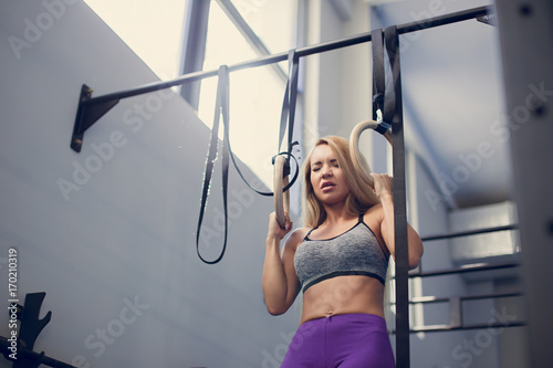 Zdjęcie XXL piękny fitness kobieta trening fitness gimnastyczne pierścienie słoneczny zewnątrz. Sporty dziewczyna robi siedzieć podnosi na gimnastycznych pierścionkach