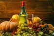 a bottle and a glass of grape wine and bright pumpkins, grapes and apples on branches and grass on a wooden background. holiday halloween a bottle and a glass of grape wine and bright pumpkins, grapes and apples on branches and grass on a wooden background. holiday halloween