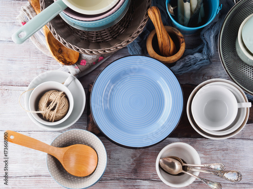 Plakat Ceramiczna i emaliowa crockery tableware na drewnianym tle. Pastelowe kolory vintage. Niebieski pusty talerz na tekst
