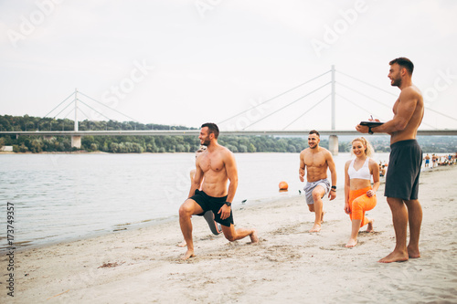 Plakat Grupują młodych atrakcyjnych ludzi ma zabawę na plaży i robi niektóre sprawności fizycznej trening.