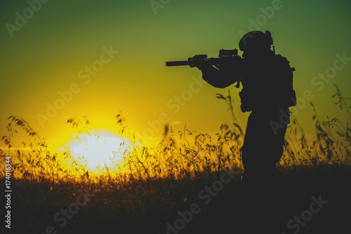 Fotoobraz na płótnie Sylwetka militarny żołnierz z broniami przy zmierzchem. strzał, trzymając pistolet, kolorowe niebo. koncepcja wojskowa.