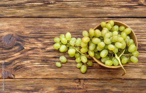 Bowl with fresh ripe green grapes on wooden background. Top view.