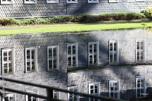 Spiegelung einer Fensterfront eines Schieferhauses/ Fassade aus Schiefer im Wasser