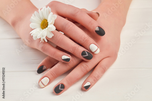 Plakat Zadbane dłonie i biała chryzantema. Kobiet ręki z matte manicure i małym kwiatem na białym drewnianym tle. Leczenie paznokci i spa.