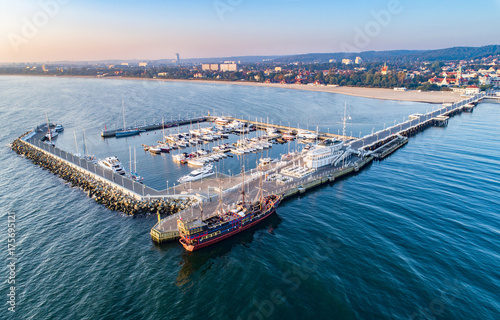 Zdjęcie XXL Sopot Resort w Polsce. Drewniane molo (molo) z mariną, jachtami, pirackim statkiem turystycznym, infrastrukturą plażową i wakacyjną. Widok z lotu ptaka na wschód słońca