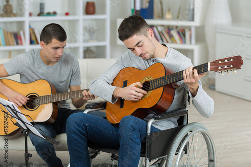 Fotoobraz na płótnie Młodzi mężczyźni grają na gitarze, jeden na wózku inwalidzkim