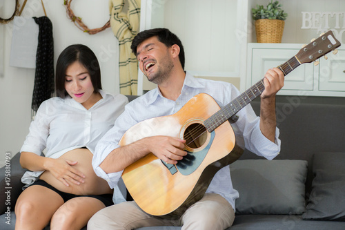 Plakat Mąż gra gitara i piękna mama w ciąży w salonie na kanapie, rodziny i zrelaksować się koncepcja.