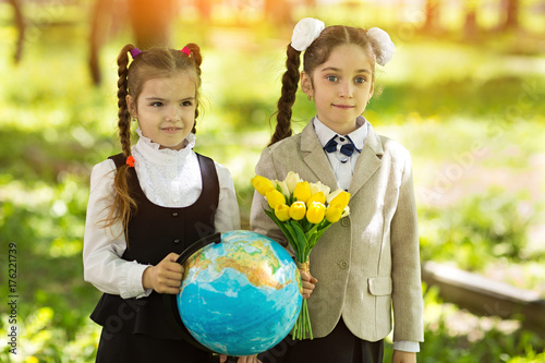 Plakat Koncepcja - edukacja. Powrót do szkoły. Dwa wesołej kaukaska dziewcząt uczennice z kwiatami i globusem, szczęśliwy, że wracają do domu po zajęciach w klasie