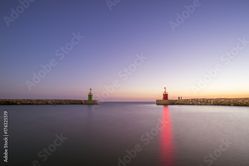 Zdjęcie XXL Seascape dwa mała latarnia morska z ich odbiciami na morzu przy zmierzchem. Niektórzy ludzie łowią pod rozgwieżdżonym niebem. Fotografia brać przy zmierzchem w Sabaudia plaży, Włochy