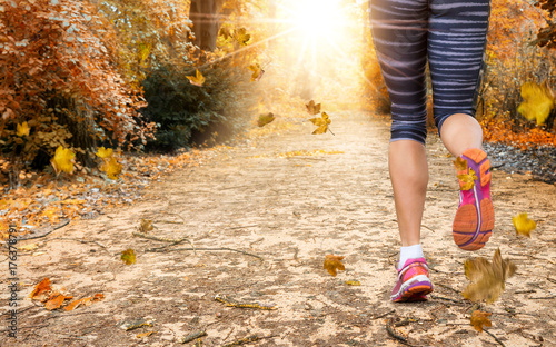 Beine einer weiblichen Joggerin im herbstlichen Park mit herabfallendem Laub
