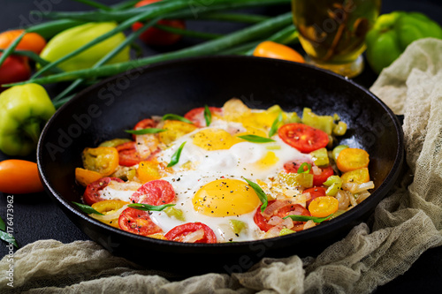Fotoobraz na płótnie Smażący jajka z warzywami - shakshuka w smaży niecce na czarnym tle
