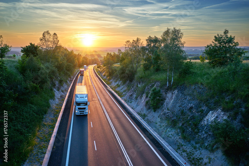 Zdjęcie XXL Trzy ciężarówki jedzie na autostradzie w wiejskim krajobrazie przy zmierzchem. Widok z góry.