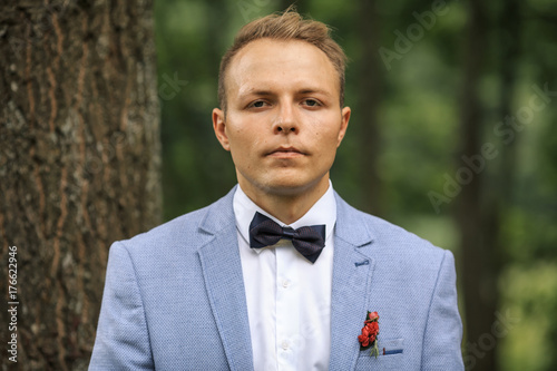 Plakat Młody przystojny fornal w niebieskiej marynarce pozuje na ślubnym spacerze w lesie. Dzień ślubu.