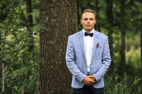 Plakat Młody przystojny fornal w niebieskiej marynarce pozuje na ślubnym spacerze w lesie. Dzień ślubu.