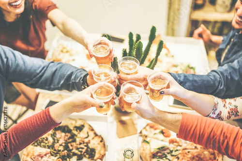 Group of friends enjoying dinner toasting with beers and eating pizza at home