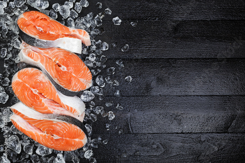 Salmon steaks on ice on black wooden table top view. Copy space