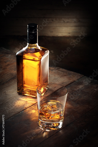 close up view of glass of  whiskey and a bottle aside on color background 