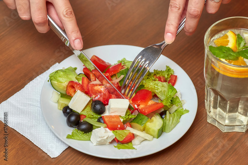 Hands with fork and knife. Salad and drink on table