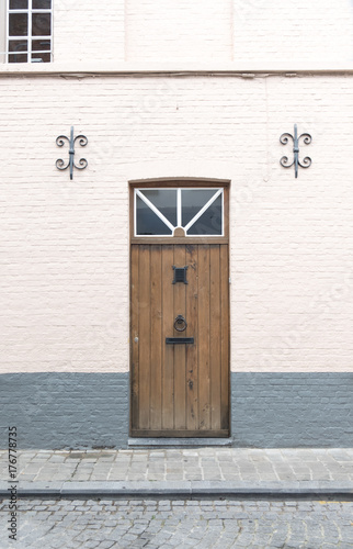 Old wooden door with metal ring knocker and mail slot on a brick building in Antwerp Belgium. Weathered wooden door on a quaint cobbled street in Europe. Anchor plates on both sides of the door
