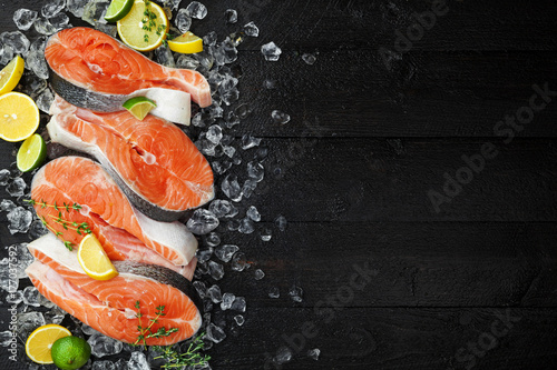 Salmon steaks on ice on black wooden table top view. Fish food concept. Copy space