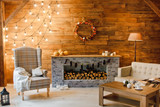 Home comfort. Armchair near the fireplace with firewood. Photo of interior of room with a wooden wall, wreath and garlands, Christmas atmosphere