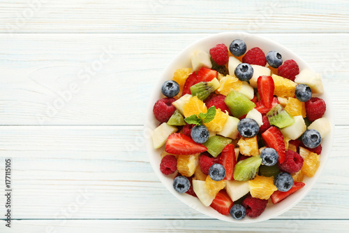 Fresh fruit salad in bowl on white wooden table