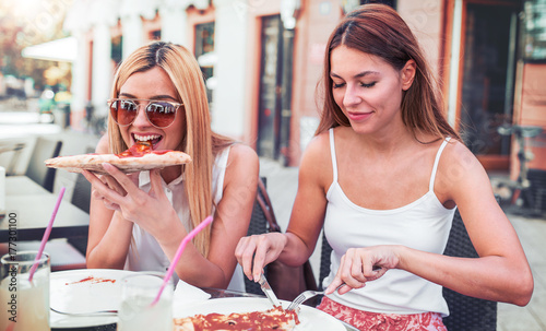 Plakat Czas pizzy. Młode dziewczyny je pizzę w kawiarni. Konsumpcjonizm, styl życia