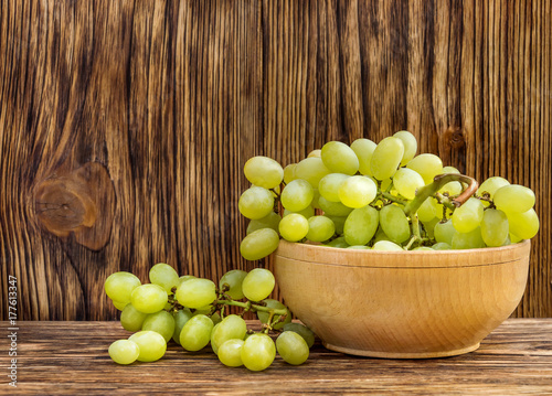 Bowl with fresh ripe green grapes on wooden background.
