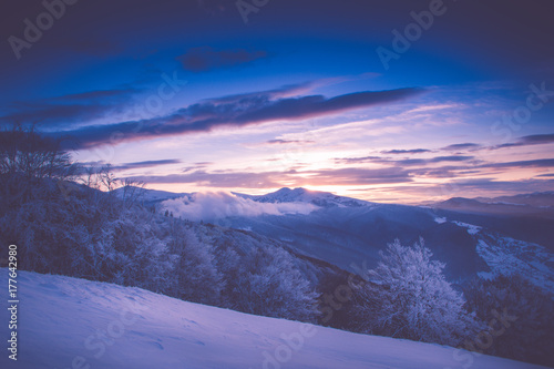 Beautiful sunrise in the winter mountains. Dramatic cloudy over sky. View of foggy hills  and trees covered with rime. Filtered image:cross processed retro effect.