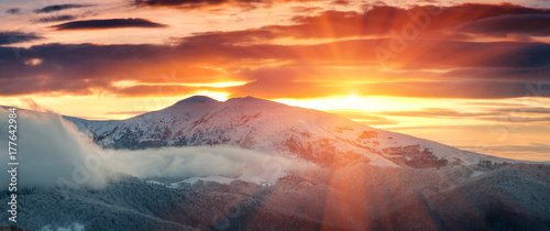 Panoramic view of winter mountains at sunrise. Landscape with foggy hills and trees covered with rime. Dramatic cloudy over sky. 