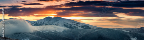 Panoramic view of winter mountains at sunrise. Landscape with foggy hills and trees covered with rime. Dramatic cloudy over sky. 