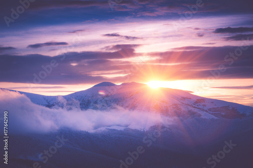Beautiful sunrise in the winter mountains. Dramatic cloudy over sky. View of foggy hills  and trees covered with rime. Filtered image:cross processed retro effect.