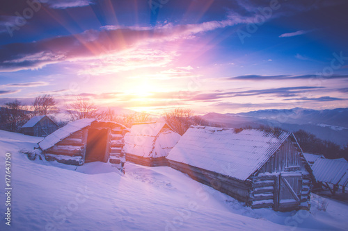 Colorful winter sunrise in the mountains. Fantastic morning glowing by sunlight. View of the snowy forest and old wooden hut cabin. Happy New Year! Filtered image:cross processed retro effect.