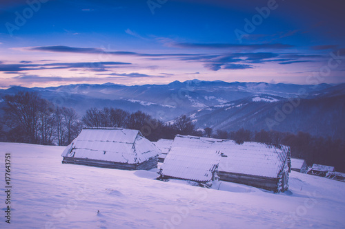 Colorful winter sunrise in the mountains. Fantastic morning glowing by sunlight. View of the snowy forest and old wooden hut cabin. Happy New Year! Filtered image:cross processed retro effect.