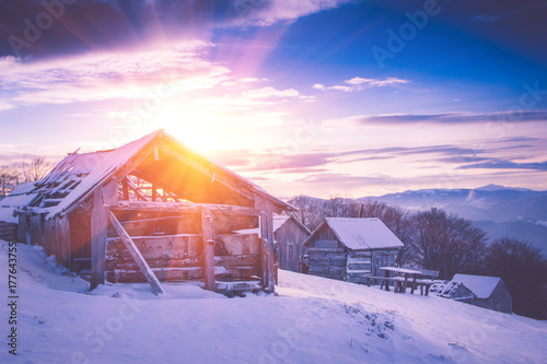 Colorful winter sunrise in the mountains. Fantastic morning glowing by sunlight. View of the snowy forest and old wooden hut cabin. Happy New Year! Filtered image:cross processed retro effect.
