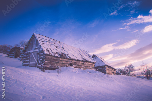 Colorful winter sunrise in the mountains. Fantastic morning glowing by sunlight. View of the snowy forest and old wooden hut cabin. Happy New Year! Filtered image:cross processed retro effect.