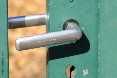 Verkratzte Türklinke eines grünen Gartentores