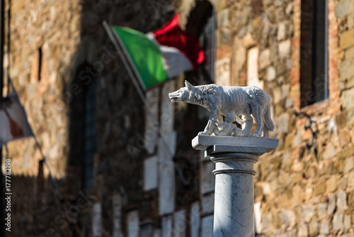 Zdjęcie XXL Rzeźba wilczyca ssąca niemowlęta Romulus i Remus, z włoską banderą w tle, Montalcino, Włochy.