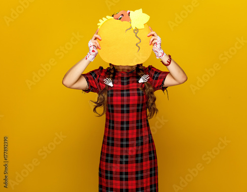 woman on yellow background holding pumpkin in front of face