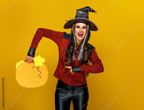 happy woman isolated on yellow background pointing at pumpkin