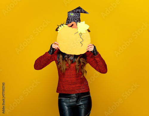 woman on yellow background holding pumpkin in front of face