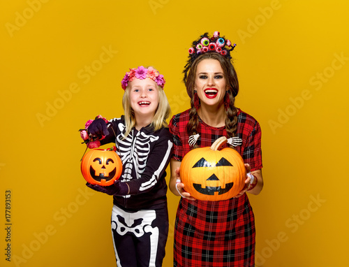 smiling mother and daughter showing jack-o-lantern pumpkins