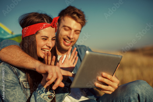 Happy young couple uses a digital tablet on sunny day in nature