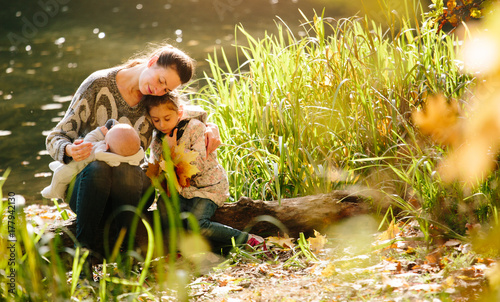 Motherhood concept. Mother and children hugging and lining each other while sitting next to a lake