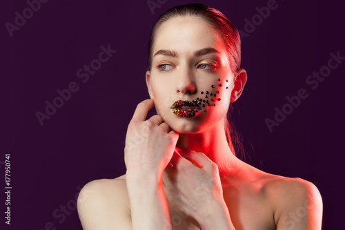 Young beautiful girl with blue eyes. Bright makeup, red lipstick. Art, rhinestones on the lips and face