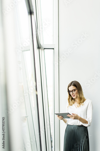 Young businesswoman standing wirth tablet in the office by window
