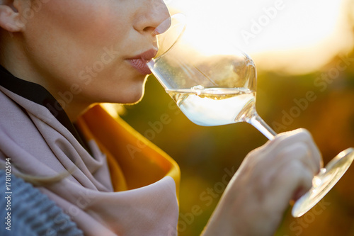Close up of a woman tasting a glass of white wine in autumn vineyard
