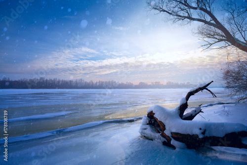 winter landscape panorama; sunset on the bank of a frozen river; ice and snow